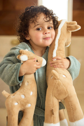 Child holding two plush giraffe toys in a home setting